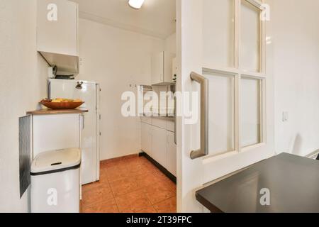 Small kitchen with white cabinets and appliances seen through entrance with sliding doors at apartment Stock Photo
