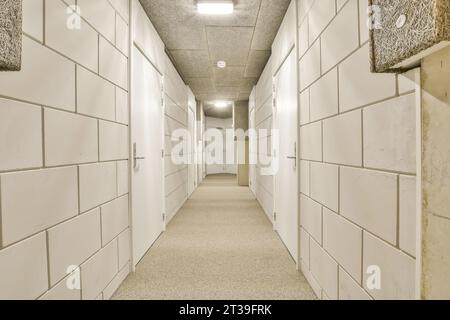 Long narrow corridor with white tiled doors with closed doors of storage rooms in industrial building for rental Stock Photo