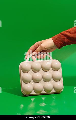 Crop hand of anonymous person holding cream color plastic golf ball box placed on green surface with bright sunlight in background outside Stock Photo