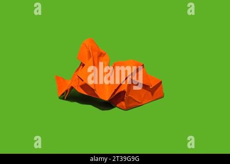 A vibrant orange paper folded figure set against a bright green background. Stock Photo