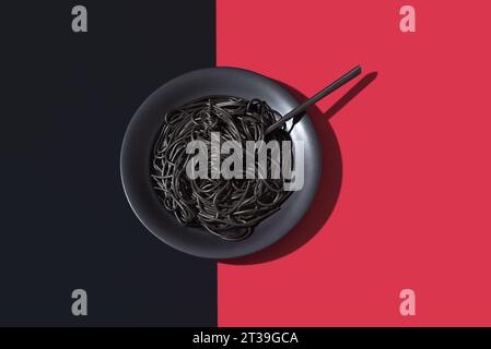 Top view of black spaghetti in a bowl with fork placed on black and red background Stock Photo