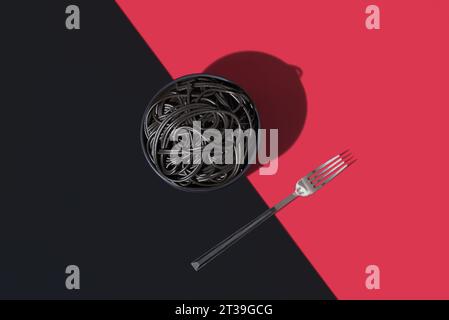 Top view of black spaghetti in a bowl placed on black and red background near fork Stock Photo