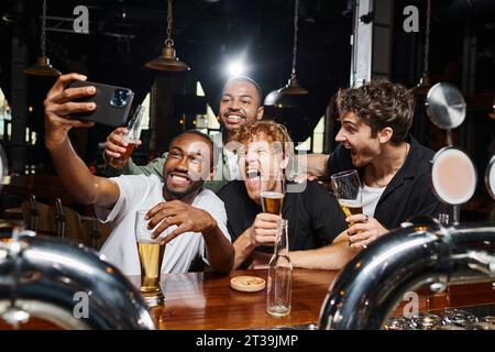 happy multicultural men taking selfie on smartphone while drinking beer in bar, bachelor party Stock Photo