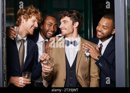 bachelor party, portrait of happy interracial best men and groom standing with glasses of whiskey Stock Photo