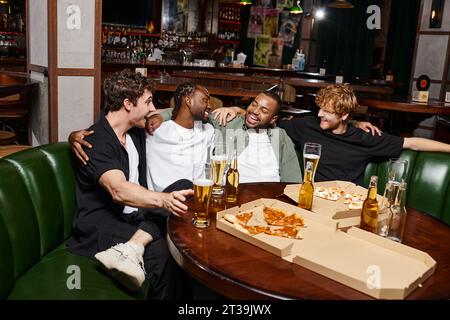 four happy interracial friends hugging and chatting near pizza and beer, spending time in bar Stock Photo