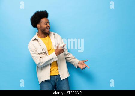 Surprised Afro African American man smiling with hands pointing to copy space aside in light blue color studio shot isolated background Stock Photo