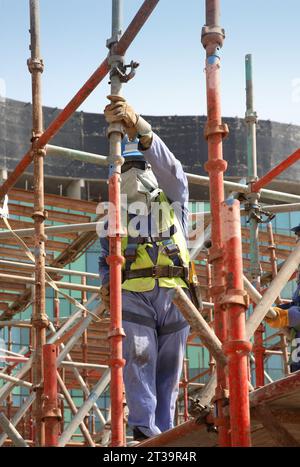 Foreign workers from India and Pakistan assemble scaffolding on a large construction site in Abu Dhabi, UAE. Stock Photo