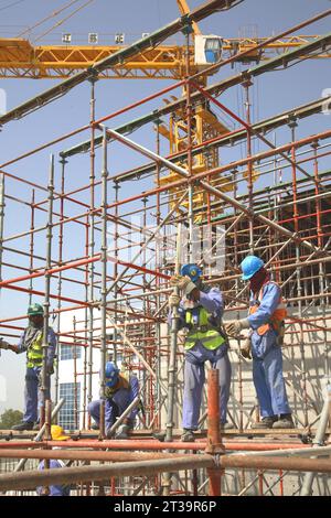 Foreign workers from India and Pakistan assemble scaffolding on a large construction site in Abu Dhabi, UAE. Stock Photo
