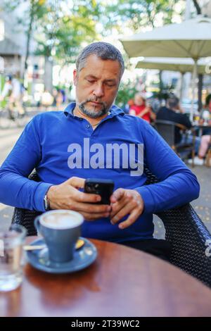 man uses smart phone while having drinks coffee in cafe outside Stock Photo