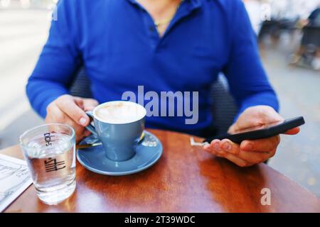 man uses smart phone while having drinks coffee in cafe outside Stock Photo