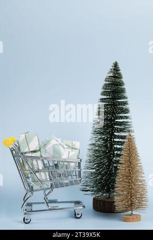 Set with a caddy filled with gifts against a luminous sky-blue background, as well as gold and green Christmas trees.  Minimalist, trendy still life p Stock Photo