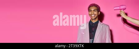 smiley man posing unnaturally on pink backdrop with closed eyes, hand with hairdryer, banner Stock Photo