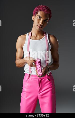 handsome pink haired male model with silver accessories and pink suspenders holding pink toy gun Stock Photo