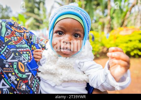 Cute healthy little African baby boy carried in an adult's arm looking at the camera. Stock Photo