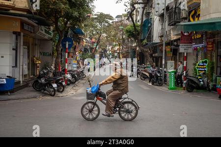 An elderly Vietnamese man rides his bicycle in Hang Bac, in the Old Quarter of Hanoi, Vietnam Stock Photo
