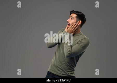 Shocked Caucasian man looking sideways with hands on cheeks in light gray isolated background studio shot Stock Photo