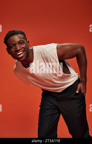 joyful african american man with hand in pocket leaning forward and smiling at camera on red Stock Photo