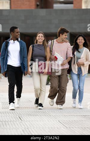 Diverse group of friends walking in the street with folder looking at camera. Multiracial young students smiling staring at camera with confidence and Stock Photo