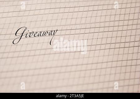 word giveaway is written with an ink pen on a white paper sheet with stripes drawn. stationery close up top view. spelling lessons and caligraphy exer Stock Photo