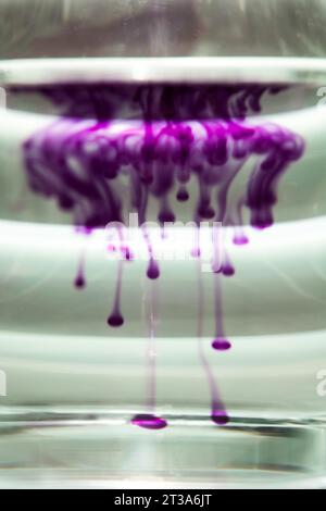 diffusion of blue ink in a transparent glass cup with clear water against the background of a striped screen with rays of light. Template, layout, bac Stock Photo