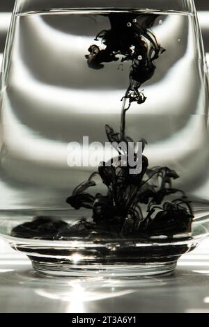a cloud of ink in a transparent glass cup with clear water against the backdrop of a striped screen with rays of light. Template, layout, background, Stock Photo
