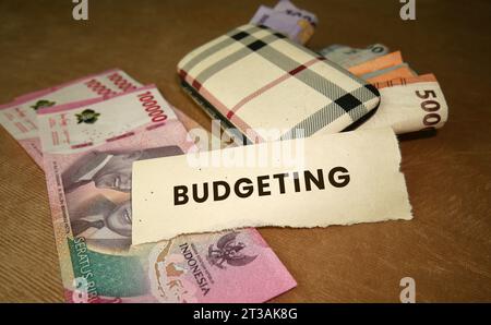 The word budgeting on a torn piece of paper with money in the background. Indonesian Rupiah. Budgeting concept. copy space Stock Photo