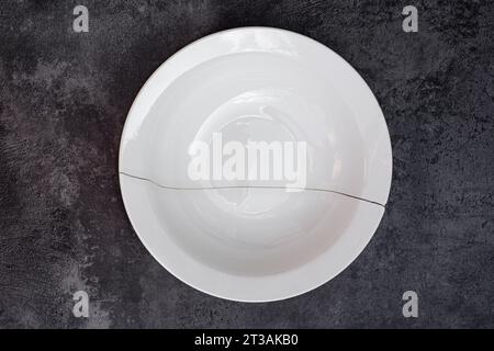 Broken white plate on a stone surface. Large crack on the dishes. Stock Photo