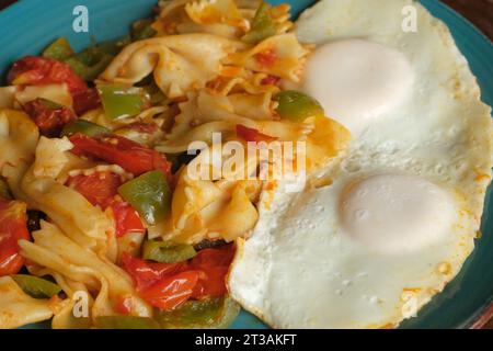 Close up dish of pasta farfalle, scrambled eggs, bacon and vegetables on a blue ceramic plate on the wooden table. Rustic breakfast on a village resor Stock Photo