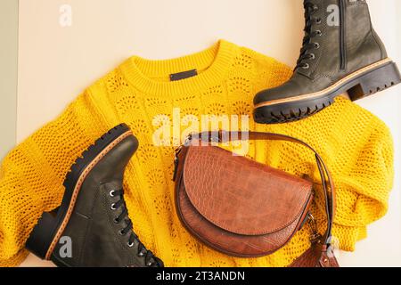 Flat lay of woman's yellow sweater and brown bag, pair of boots on neutral beige background. Autumn fashion concept. Top view, flat lay. Stock Photo