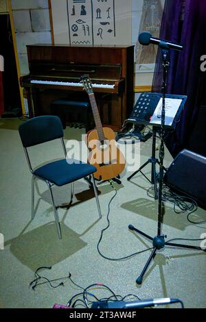 An image of an acoustic guitar stands on stage near a music stand Stock Photo