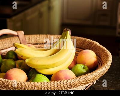 Fresh bananas in the basket with various fruits on the kitchen counter. Stock Photo