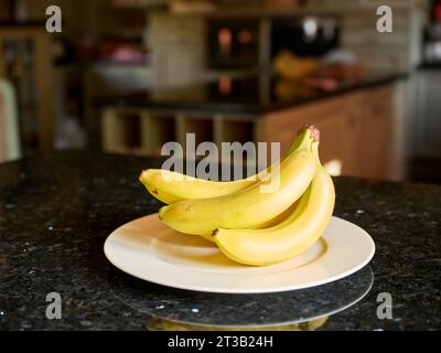 Fresh bananas on a white plate over black granite kitchen counter. Stock Photo
