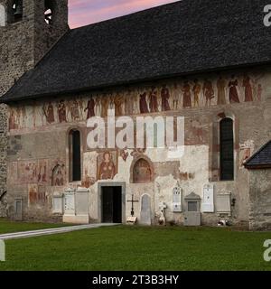 Southern facade of the Chiesa di San Vigilio (Church of Saint Vigil or Vigilius) in Pinzolo, Trentino-Alto Adige, Italy.  Running along the top of the wall, below the eaves, is a Danza Macabra (Dance of Death) fresco frieze, painted in 1539 by Simone II Baschenis (c. 1495-1555). The frieze procession begins on the left:  a crowned figure of Death plays the bagpipes, accompanied by two other skeletons playing horns; they are followed by Christ on the cross and then a line of people representing very different positions in society, each pierced with the arrow of Death by a smiling skeleton. Stock Photo