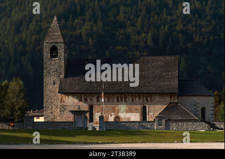 Viewed from the south, the Chiesa di San Vigilio in Pinzolo, Trentino-Alto Adige, Italy.  Below the eaves is a Dance of Death fresco frieze, painted in 1539 by Simone II Baschenis (c. 1495-1555), depicting (from left):  three skeletons playing musical instruments; Christ on the cross; 18 people with different positions in society, each pierced by the arrow of Death, with skeletons; Death on a galloping horse; and finally, the Archangel Michael and the devil holding a book on which the deadly sins are written. The church is believed to date from the 1200s and was rebuilt in 1515. Stock Photo