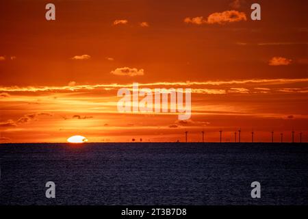 Sun dipping down past horizon over English Channel with Rampion Wind Farm Turbines silhouetted against fiery sky. Stock Photo