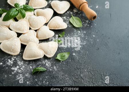 Italian ravioli pasta in heart shape. Tasty raw ravioli with flour and basil on dark background. Food cooking ingredients background. Valentines or Mo Stock Photo