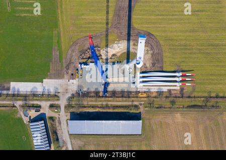 Aerial view over construction site showing rotor blades on the ground and building crane assembling steel tower sections of wind turbine at windfarm Stock Photo