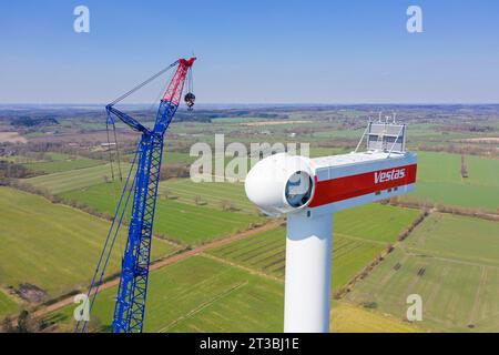 Construction crane assembling wind turbine at windfarm showing mounted nacelle with rotor hub Stock Photo