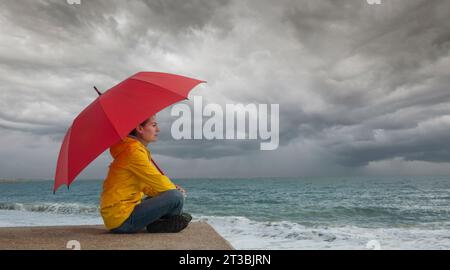 Woman with red umbrella watching storm clouds over the ocean, stormy weather concept Stock Photo