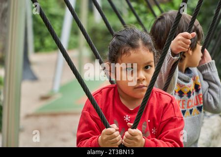 confident latin girl and boy playing on a swing on the park in Christmas holidays Stock Photo
