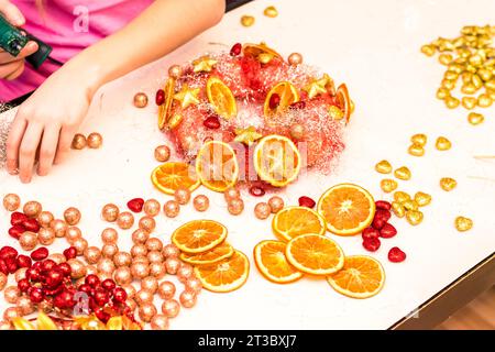 cute girl creating christmas wreath adorned with baubles and other colorful glittering decorations Stock Photo