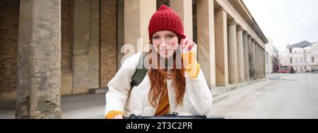 Smiling redhead european girl drives public e-scooter, tourist explores city, rides in city centre Stock Photo