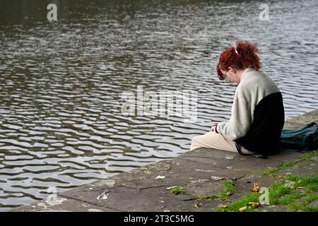 Lone woman with head down sitting on quayside wall with water in background, UK Stock Photo