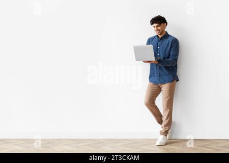 Young Arab Guy Using Laptop Leaning On White Studio Wall Stock Photo