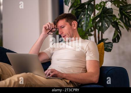 Workaholic entrepreneur man freelancer self-employed working on laptop sitting on couch at home. Stock Photo