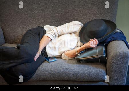 Woman with hat covering her face sleeping on couch Stock Photo