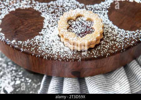 Close-up of one Linzer cookie dusted with powdered sugar on round wood board Stock Photo