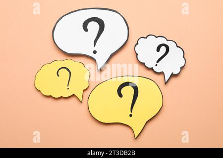 Paper speech bubbles with question marks on beige background, flat lay Stock Photo