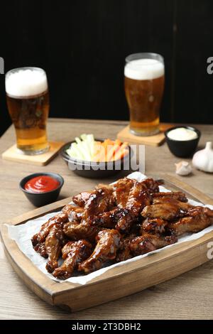 Tasty chicken wings, sauces, vegetable sticks and glasses of beer on wooden table. Delicious snacks Stock Photo