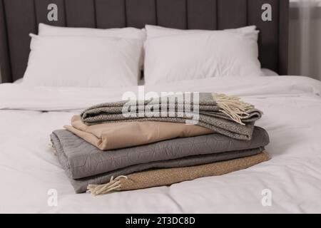 Stack of different folded blankets on bed in room. Home textile Stock Photo